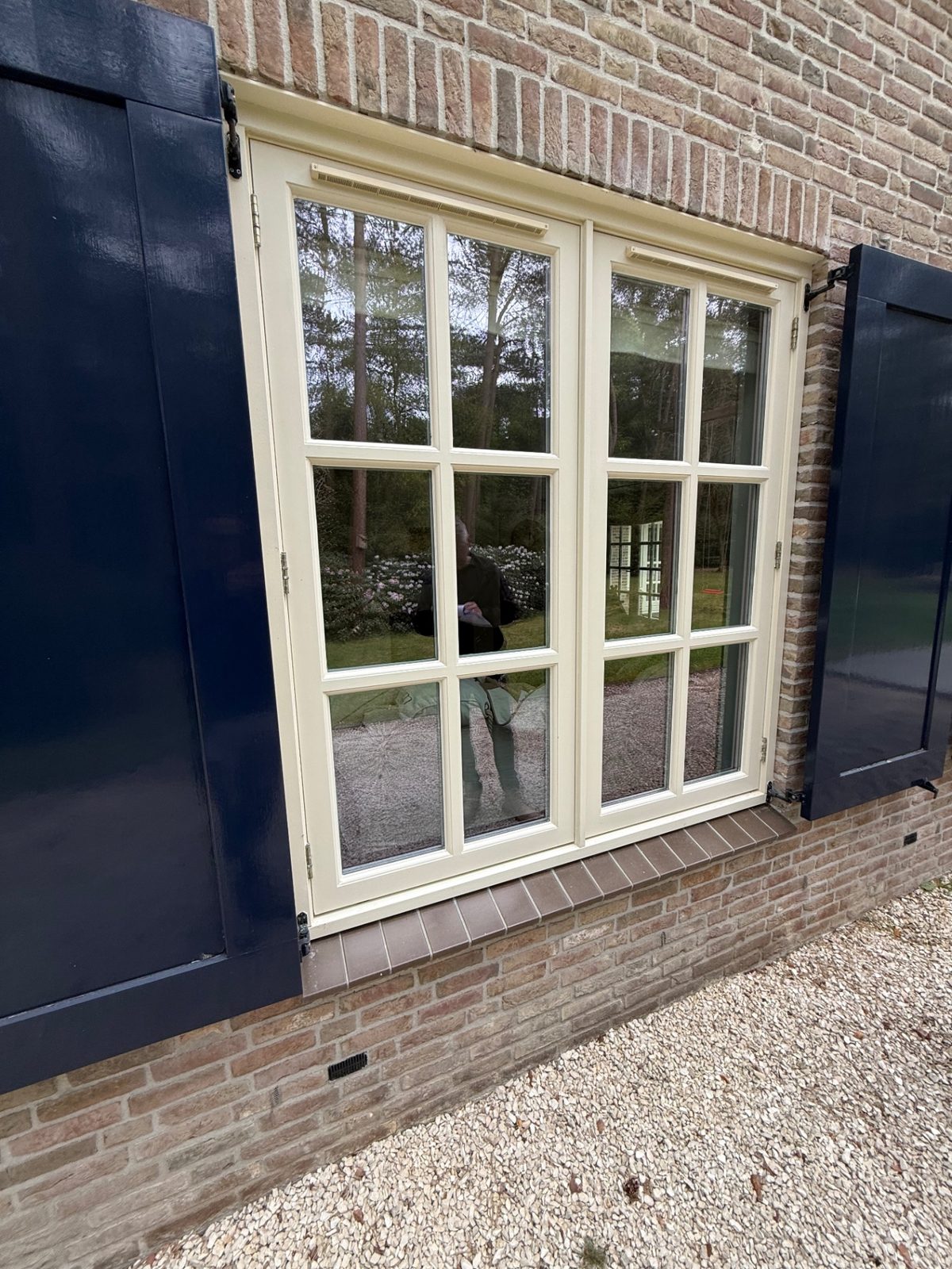 Wit raam in bakstenen gevel met donkere luiken